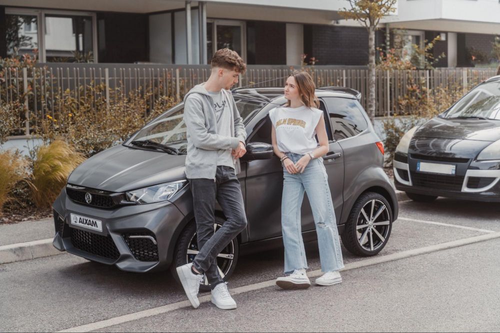 una pareja de adolescentes con su coche sin carnet delante del instituto